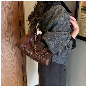 Detail view of brown suede underarm bag with white plaid stitching and metal chain trim