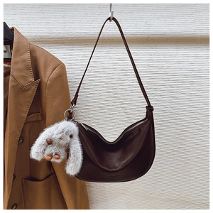 Detail of dark brown hobo shoulder bag featuring a cute plush bunny charm and embossed logo