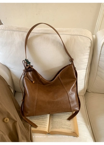 Sac hobo vintage marron avec surpiqûres en V et pendentif gland sur un canapé
