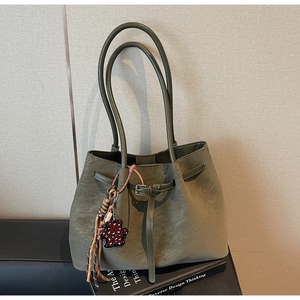 Close-up of olive green suede tote bag with leopard bear charm on design books