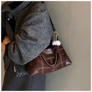 Close-up of brown suede crossbody bag featuring white grid stitching and golden chain detail