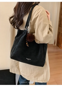 Detail of black suede tote bag with white text and brown pom-pom charm on metal ring
