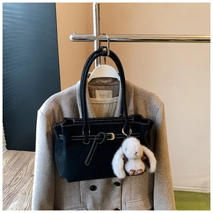 Detail of black tote bag with white stitching, decorative buckle, and plush bunny charm