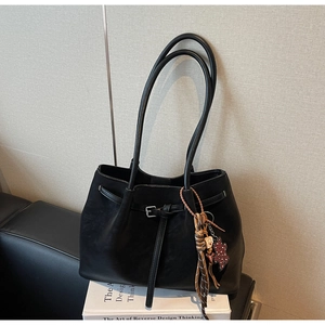 Detail of matte black leather tote bag with long handles and stylish patterned charm