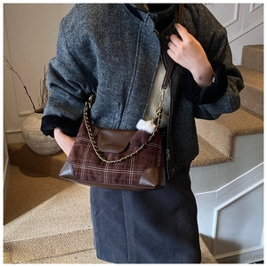 Close-up of brown plaid crossbody bag with chain handle and pompom on wool coat