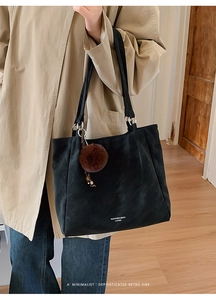 Close-up of black leather tote bag with brown pompom charm worn with a beige trench coat