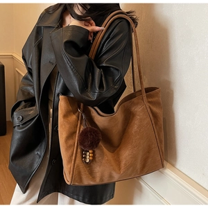Detail of vintage brown suede tote bag with fur ball and wooden bead charm accessory