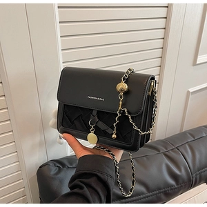 Detail of black leather square bag showing gold chain strap and woven texture bottom