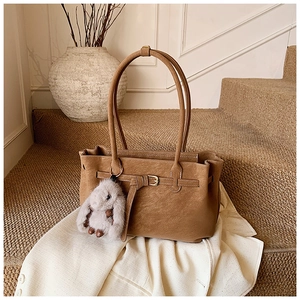 Detailed view of brown leather tote bag texture with decorative buckle and plush rabbit charm