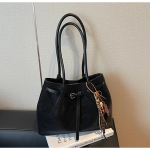 Detail view of black leather tote bag with long straps and ethnic tassel charm