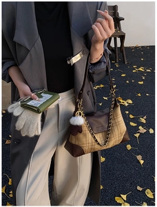Close-up of retro plaid shoulder bag with brown leather trim and plush ball charm detail