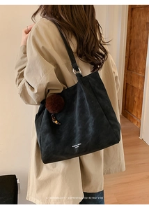 Detail of black suede tote bag featuring silver hardware and a plush pompom charm accessory