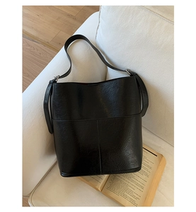 Détail du sac seau vintage noir avec texture craquelée sur un fond de canapé blanc