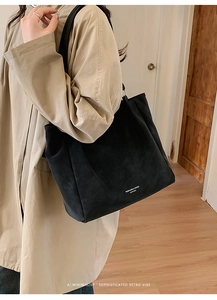 Side view of large black matte leather tote bag worn by a model in a cozy interior