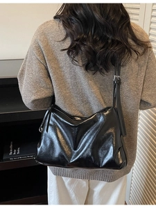 Vintage glossy black leather tote bag with adjustable strap worn by model in a street style