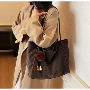 Detail of dark brown suede tote bag featuring plush ball and wooden bead charm detail