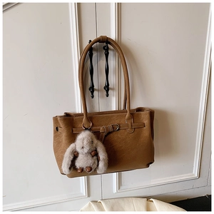 Brown leather tote bag with decorative buckle and grey plush bunny charm on white door