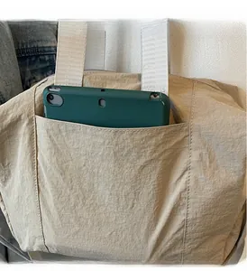 Detail view of large front pocket on beige nylon tote bag showing tablet storage capacity