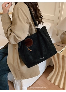 Detail of black leather tote bag featuring a brand logo and decorative brown fur ball charm