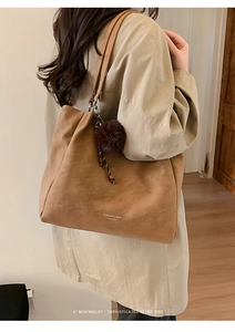 Detail of large camel tote bag with fur ball charm and leather brand logo
