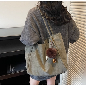 Olive green tote bag with plush charm shown in a modern urban lifestyle setting
