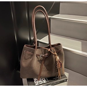 Detail of coffee brown suede tote bag with slim handles and woven tassel charm decoration