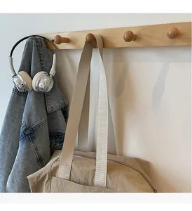 Detail of beige tote bag with nylon texture and sturdy handle hanging on wooden hook