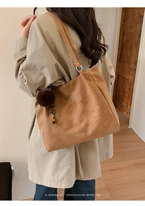 Detailed side view of a large brown retro tote bag with a plush pompom accessory