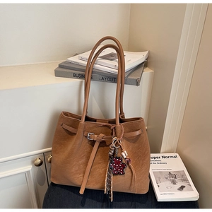 Detail of a brown leather tote bag with a metal buckle and leopard print bear charm