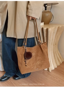 Detail of a brown suede tote bag with a dark brown pom-pom charm in a retro setting