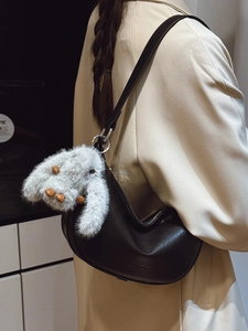 Minimalist black crescent shoulder bag with white plush bunny charm on slender strap