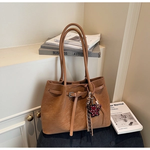 Detail of brown suede tote bag featuring a leather buckle and leopard bear charm