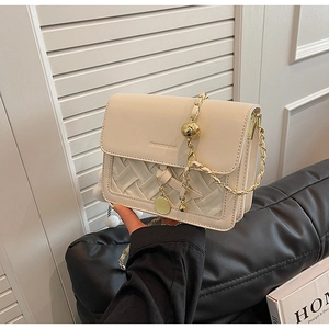 Detail of cream crossbody bag with woven texture, gold chain and metal ball charms