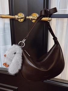 Dark brown crescent hobo bag with knotted strap and grey plush rabbit charm on a gold handle