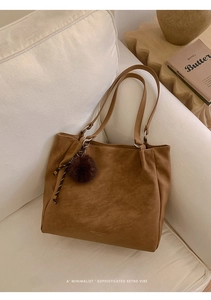 Detail of a brown suede tote bag with fur pom-pom and braided cord on a cream sofa