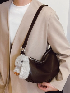 Dark brown leather half-moon hobo bag with plush rabbit pendant on a beige blazer model