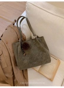 Detail of olive green leather tote bag with logo and faux fur pompom charm on a sofa