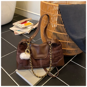 Detail of dark brown suede shoulder bag featuring contrast stitching and gold chain strap