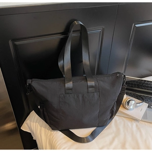 Close-up of black nylon tote bag with dual handles and adjustable strap on a bed