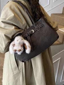 Dark brown suede tote bag with white stitching and rabbit pendant worn by model