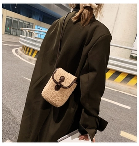 Detail of beige faux shearling crossbody bag with brown leather trim worn by model