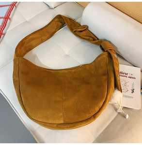 Détail d'un sac demi-lune en daim fauve avec bandoulière nouée sur un canapé blanc
