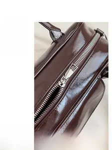 Detailed close-up of smooth silver zipper on a dark brown glossy faux leather handbag