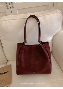 Detail of burgundy leather tote bag texture and brand logo on a soft white sofa