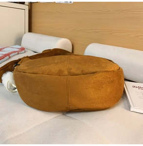 Détail du fond cousu d'un sac cabas en daim marron avec un pendentif en peluche blanc
