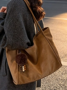 Vintage brown leather tote bag with pompom charm shown on shoulder for autumn fashion