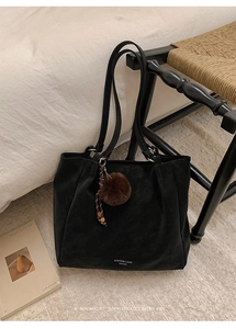 Detail of black tote bag with plush ball charm on a wooden chair in a home setting
