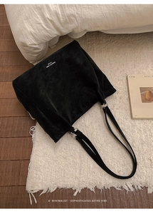 Detail of a minimalist black matte leather tote bag featuring silver metal rings on a rug