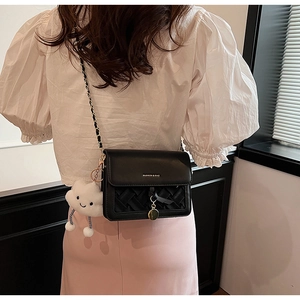 Detail of black leather crossbody bag featuring woven texture and a plush cloud charm
