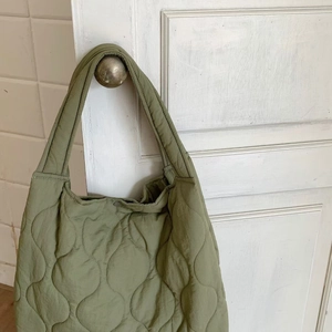 Detail of green quilted nylon tote bag with wave stitching and magnetic snap closure